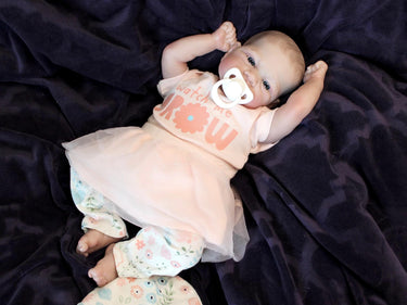 A baby doll with a pacifier lies on a cozy blanket, highlighting its charming design and soothing presence.